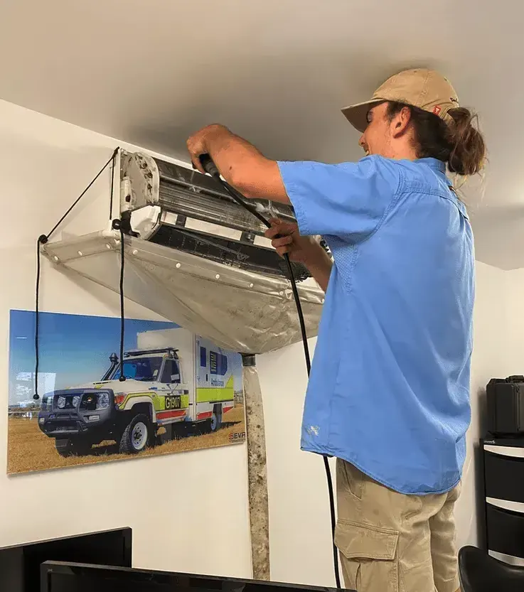 Technician inspecting a split system air conditioner as part of a cleaning assessment