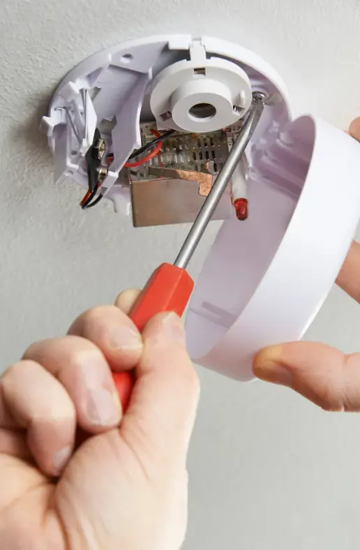 Hand pressing the test button on a household smoke alarm