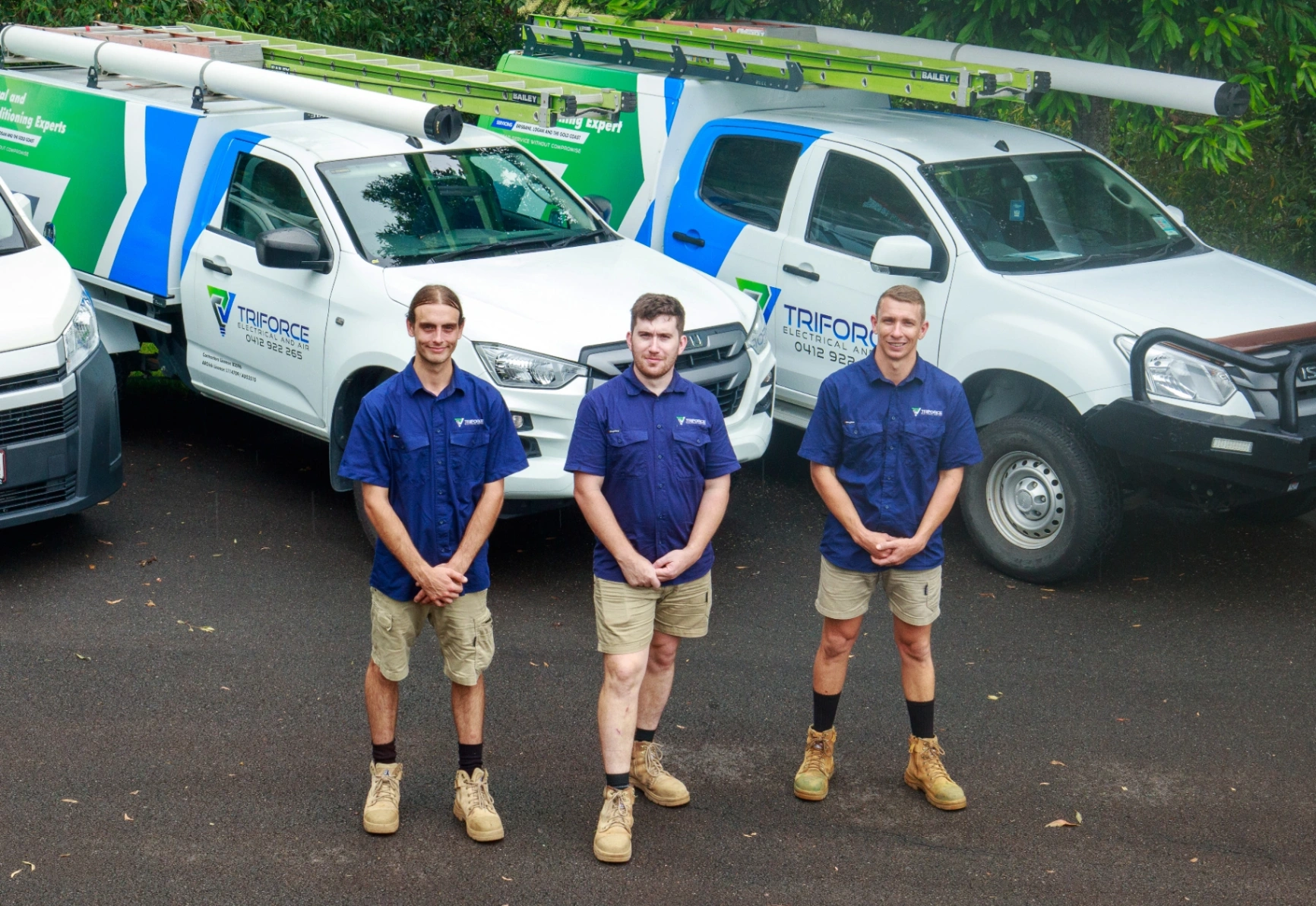 Three Triforce Electrical and Air technicians standing in front of company service vehicles